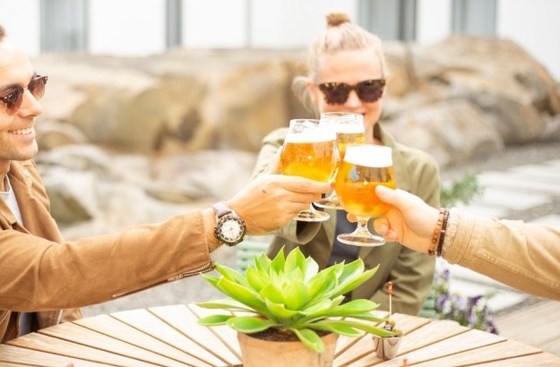 Friends enjoying a beer toast in the sunlit garden at Midgardur by Center Hotels in Reykjavik.