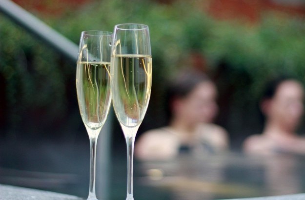 Two champagne glasses at the edge of the spa hot tub with guests relaxing in the background at Midgardur by Center Hotels.