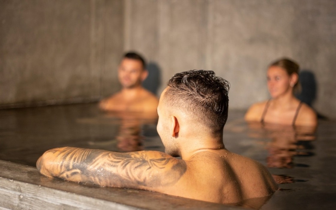 Guests relaxing in the indoor hot tub at the spa in Midgardur by Center Hotels in Reykjavik, with a warm, serene atmosphere and concrete walls.
