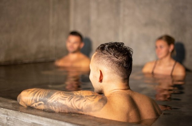 Guests relaxing in the indoor hot tub at the spa in Midgardur by Center Hotels in Reykjavik, with a warm, serene atmosphere and concrete walls.