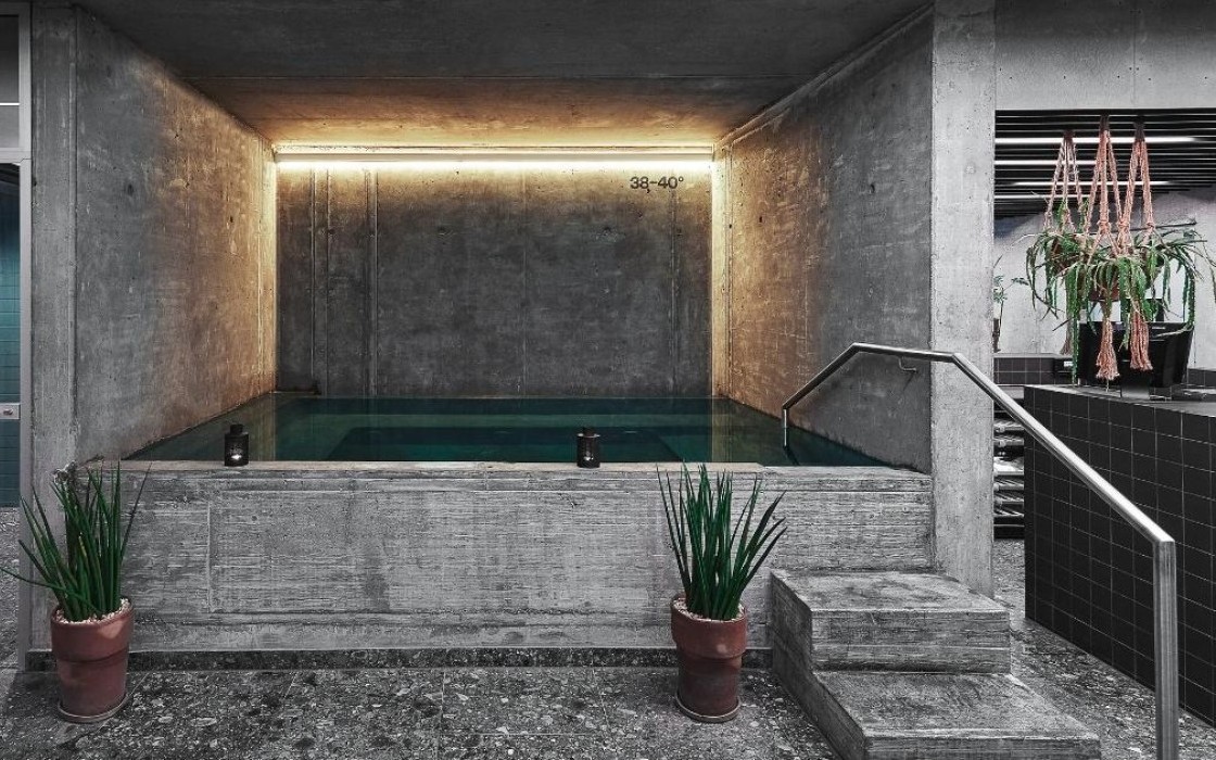 Indoor hot tub at Midgardur by Center Hotels with modern concrete surroundings, soft lighting, and potted plants.