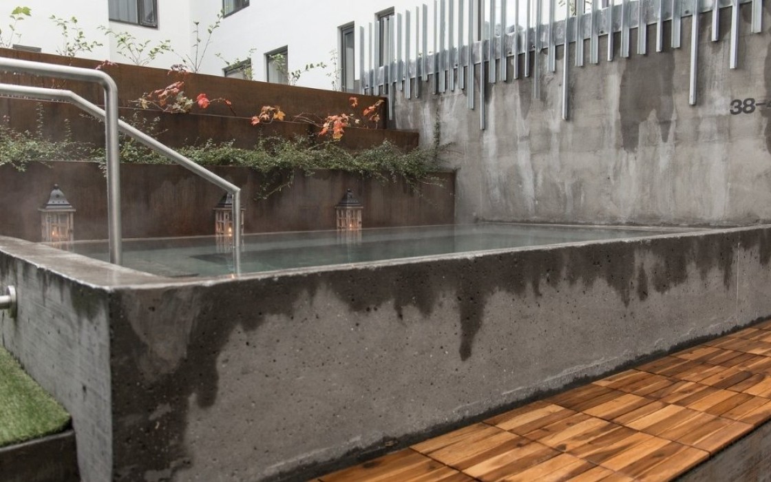 Outdoor hot tub at Midgardur spa with warm concrete design and greenery in central Reykjavik.