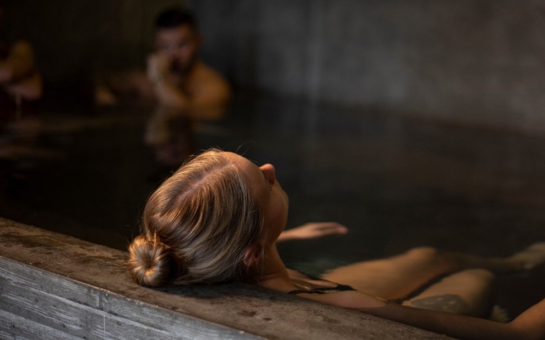 A guest relaxing in the indoor hot tub at Midgardur by Center Hotels in Reykjavik with ambient lighting and concrete walls.