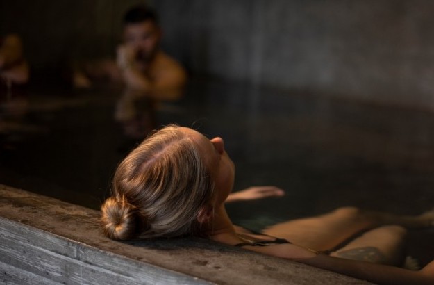 A guest relaxing in the indoor hot tub at Midgardur by Center Hotels in Reykjavik with ambient lighting and concrete walls.