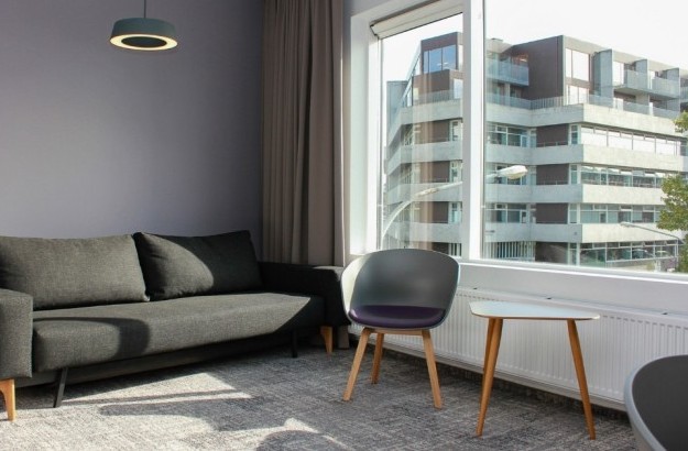 Seating area at Midgardur by Center Hotels in Reykjavik with grey sofa, chairs, and large window view.