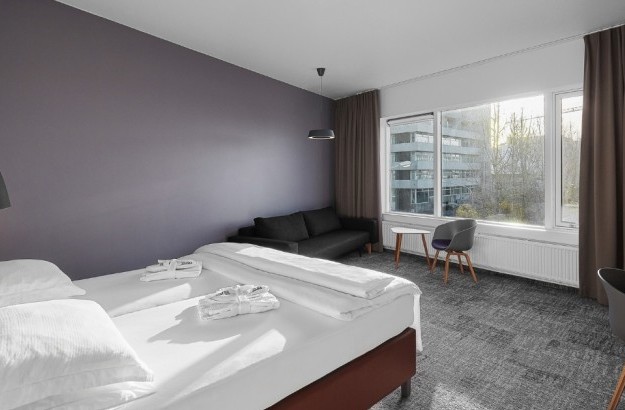 Bright deluxe hotel room in Reykjavik at Midgardur by Center Hotels with large windows, double bed, and lounge area.