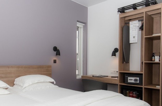 Twin bed setup with light wood headboard, integrated open closet, and compact desk in the standard room at Midgardur by Center Hotels in Reykjavik.