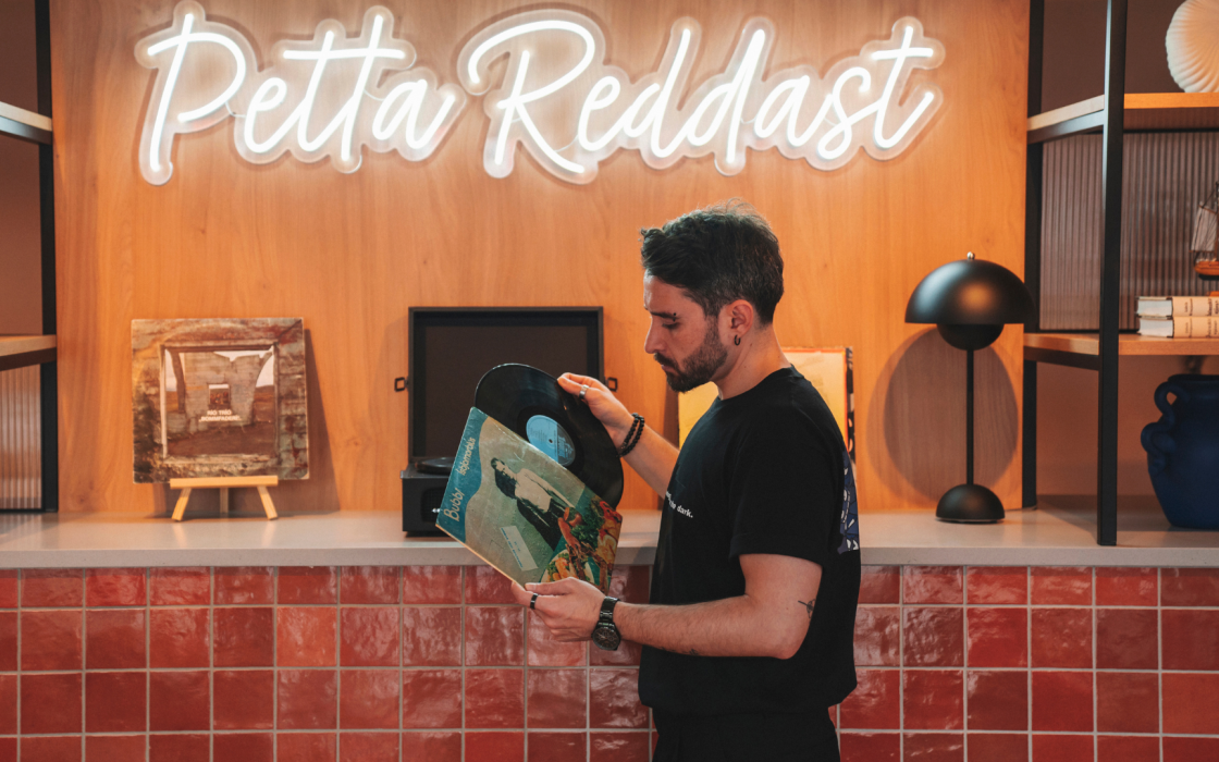A man flipping through vinyl records in a display area at Center Hotels Plaza in Reykjavík. Behind him is a glowing neon sign that reads “Þetta Reddast,” Icelandic for “It will all work out,”