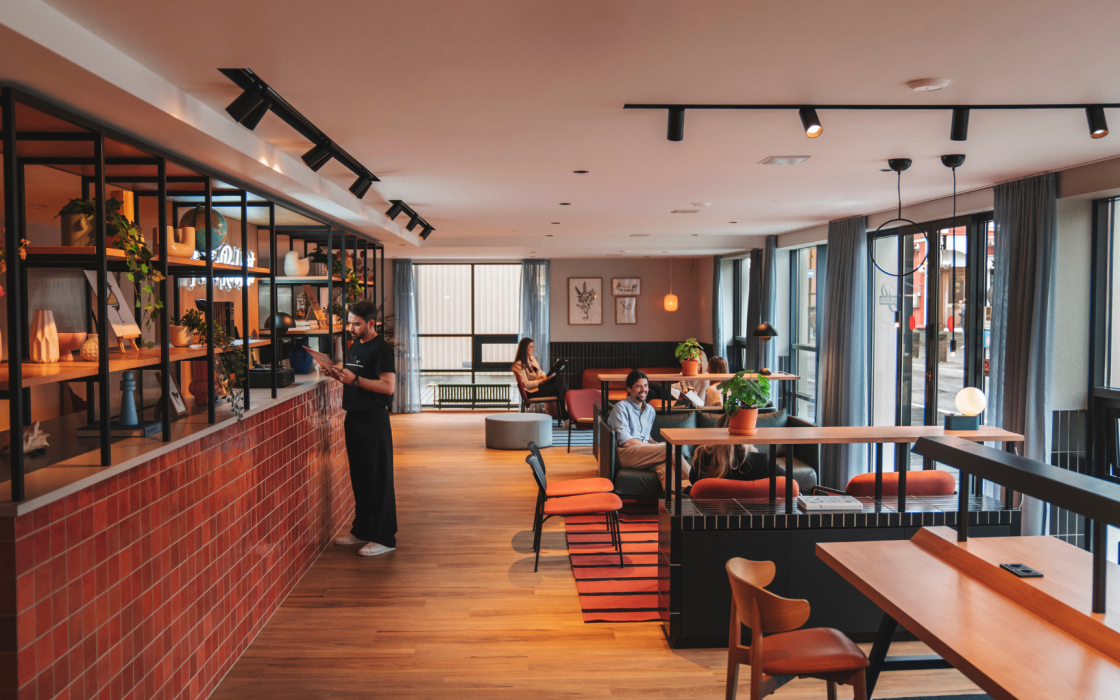 A modern lobby lounge at Center Hotels Plaza in Reykjavik, featuring warm wood flooring, comfortable seating with people relaxing, and large windows letting in natural light from the street o