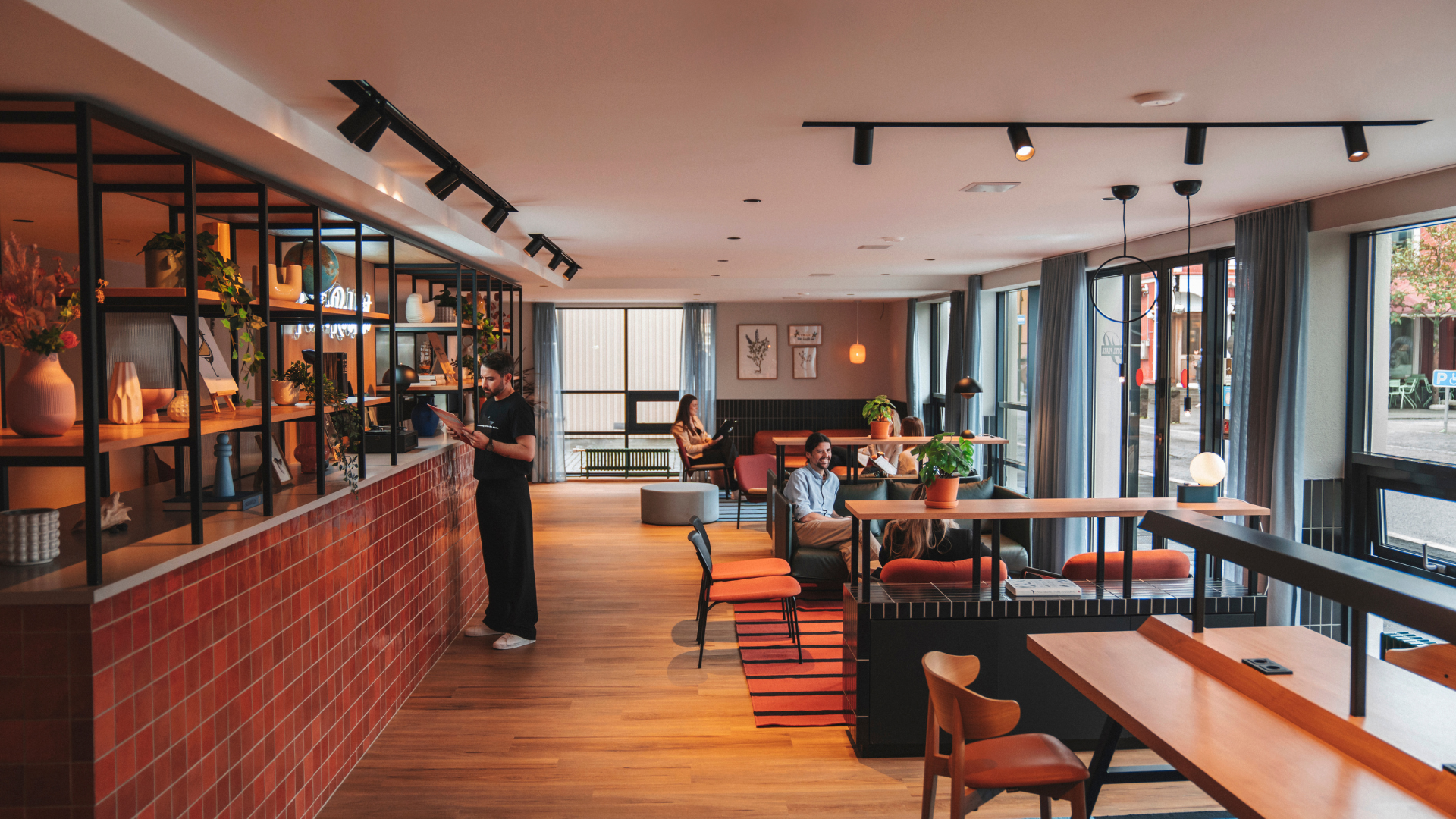 A modern lobby lounge at Center Hotels Plaza in Reykjavik, featuring warm wood flooring, comfortable seating with people relaxing, and large windows letting in natural light from the street o