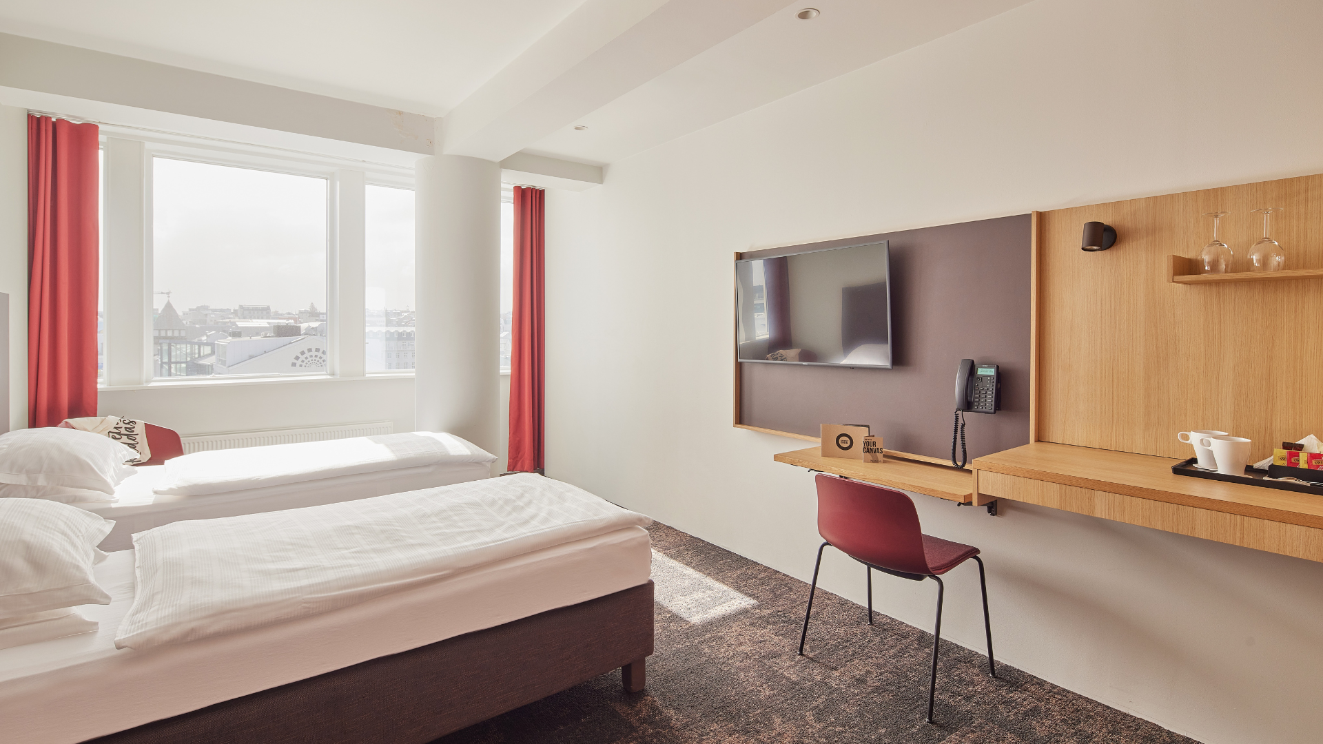 Bright and airy Superior Room at Center Hotels Plaza in Reykjavík featuring two single beds with crisp white linens, large windows with red curtains, a mounted flat-screen TV, and a minimalis