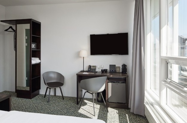 Interior of an Executive Room at Center Hotels Plaza in Reykjavík, showcasing a work desk, flat-screen TV, mini fridge, open wardrobe with safe and bathrobes, and two contemporary grey chairs