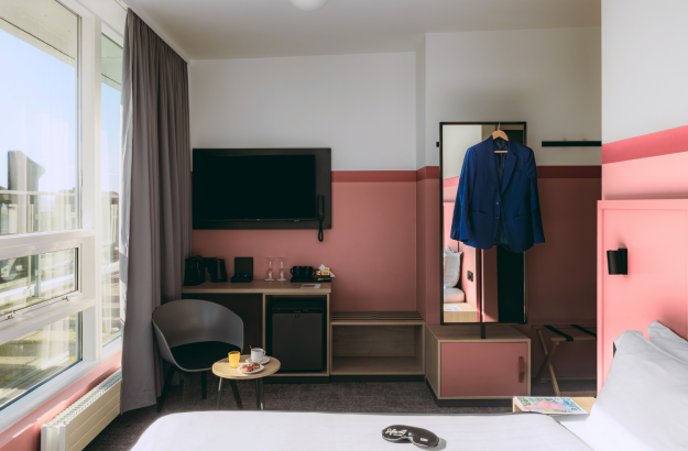 A picture of the executive room at Center Hotels Plaza in Reykjavík with pink walls, king size bed, desk, minibar, large mirror and balcony with view of the city.