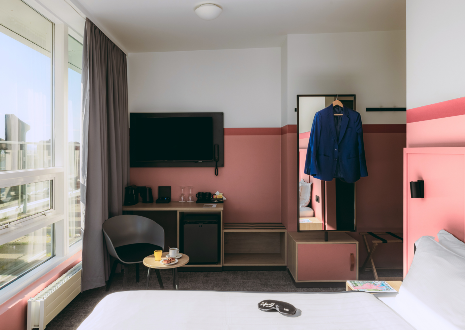 A picture of the executive room at Center Hotels Plaza in Reykjavík with pink walls, king size bed, desk, minibar, large mirror and balcony with view of the city.