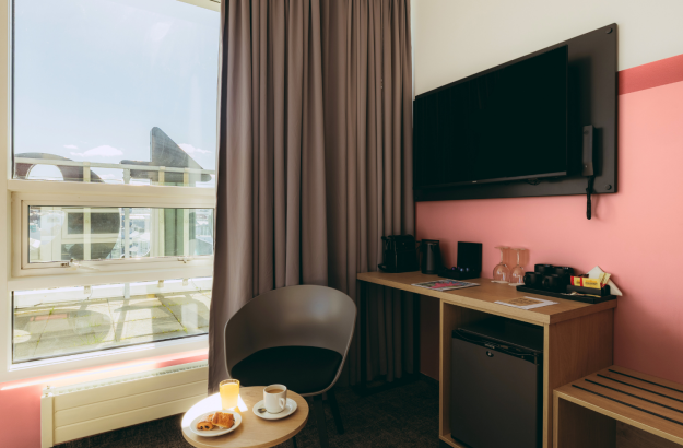 A picture inside the executive room at Center Hotels Plaza in Reykjavík where you can see a desk, minibar, a small table with breakfast and a chair, and a balcony with a view over the city ce