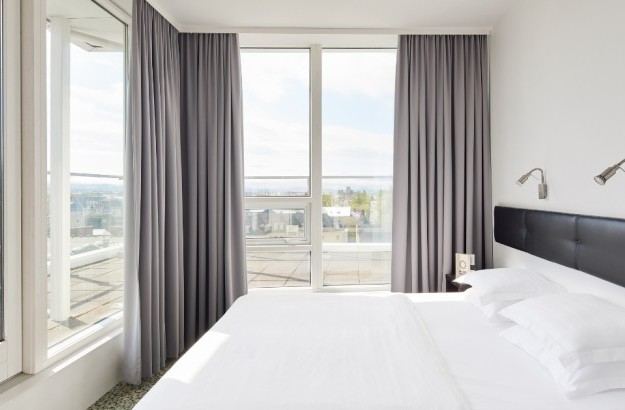 Executive Room at Center Hotels Plaza in Reykjavík with a bright corner view, featuring a double bed with white linens, floor-to-ceiling windows, and a private balcony overlooking the city ro