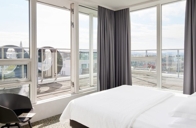 A stunning panoramic view from the Executive Room at Center Hotels Plaza in Reykjavík, seen from the bed through floor-to-ceiling windows that open onto a private terrace. The hotel's large s