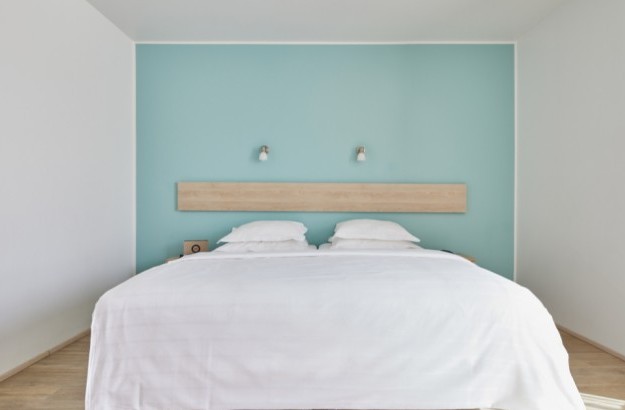 A minimal and serene Standard Room at Center Hotels Plaza in Reykjavík, featuring a double bed with crisp white linens, a pale turquoise accent wall, wooden floors with soft lighting above th