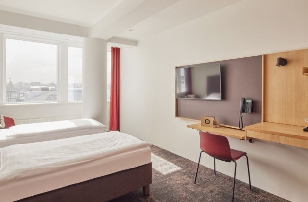Bright and airy Superior Room at Center Hotels Plaza in Reykjavík featuring two single beds with crisp white linens, large windows with red curtains, a mounted flat-screen TV, and a minimalis