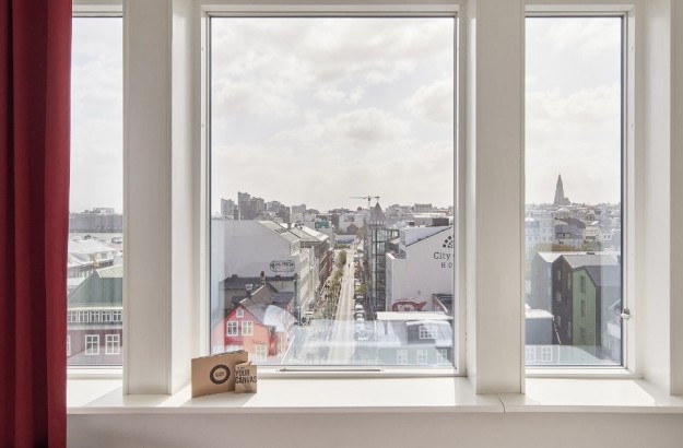 City view from a Superior Room window at Center Hotels Plaza in Reykjavík, looking out over downtown rooftops, colorful graffiti art, historic buildings, and Hallgrimskirkja church.