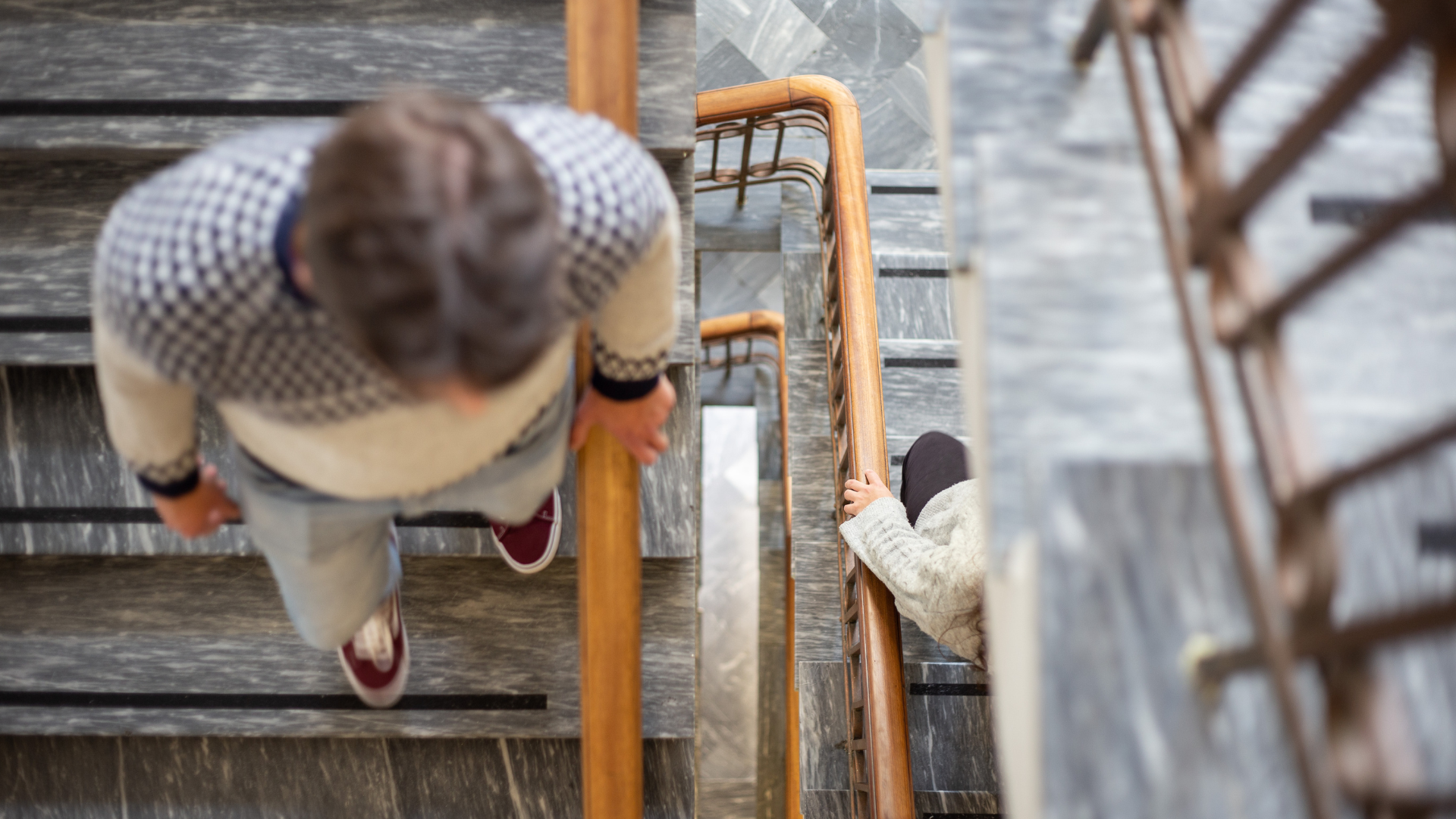Interior marble staircase at Center Hotels Skjaldbreid with guests walking up and down, featuring wooden railings and tiled steps.