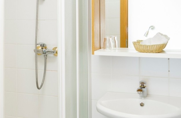 Bright bathroom in a standard single room at Center Hotels Skjaldbreid, featuring a shower, sink, mirror, and amenities in a basket.
