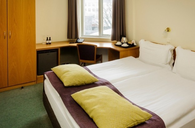 Overview of the standard room at Center Hotels Skjaldbreid in Reykjavik, featuring a double bed, a long desk with a purple chair, a wardrobe and a window with natural light.