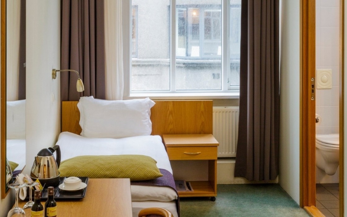 Cozy standard single room at Center Hotels Skjaldbreid in Reykjavik, with a single bed, large window, desk, coffee station, and bathroom.