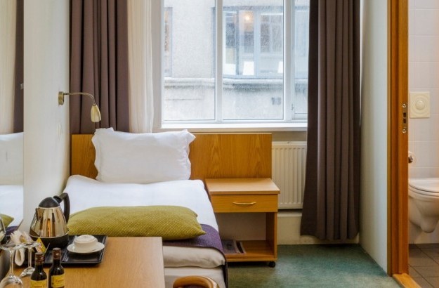 Cozy standard single room at Center Hotels Skjaldbreid in Reykjavik, with a single bed, large window, desk, coffee station, and bathroom.
