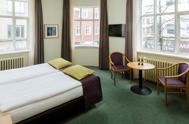 Superior room at Center Hotels Skjaldbreid with a large bed, a window, and a small table with drinks and purple chairs.