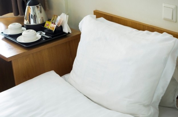 Close-up of a neatly made bed in a standard room at Center Hotels Skjaldbreid, with white bedding and an in-room tea and coffee tray on a wooden desk.