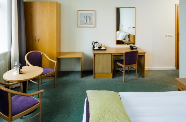 Spacious superior room at Center Hotels Skjaldbreid in Reykjavik, featuring a double bed, wardrobe, desk, mirror, and cozy seating area with purple chairs and natural light from windows.