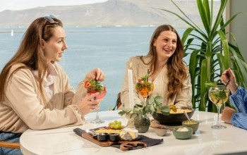 Three women sitting by a round table at Sky Bar in Reykjavik enjoying a cheese platter, nachos and cocktails.