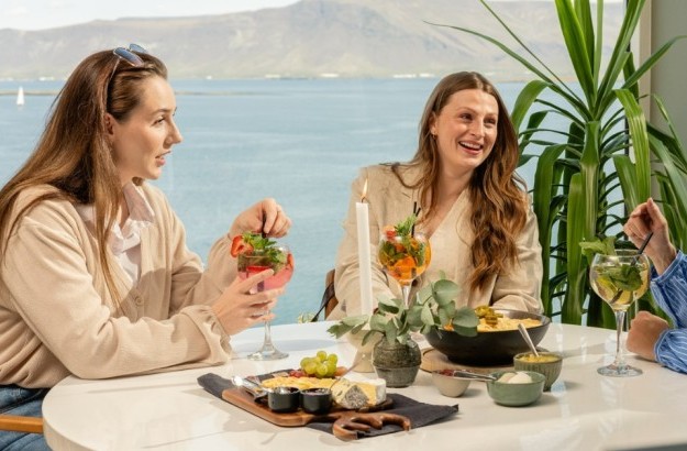 Three women sitting by a round table at Sky Bar in Reykjavik enjoying a cheese platter, nachos and cocktails.
