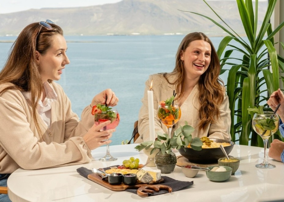 Three women sitting by a round table at Sky Bar in Reykjavik enjoying a cheese platter, nachos and cocktails.