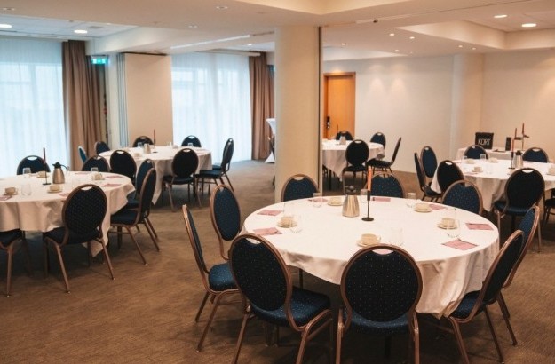 Venue setup at Center Hotels Plaza with five big round tables with blue chairs, white tablecloths and pink napkins.