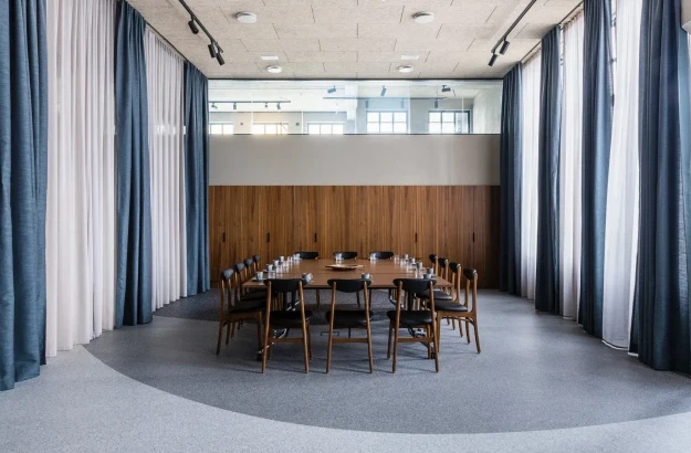 One large table in a meeting rooms with black leather seats. The room is set up for a meeting with glasses and pens on the table.