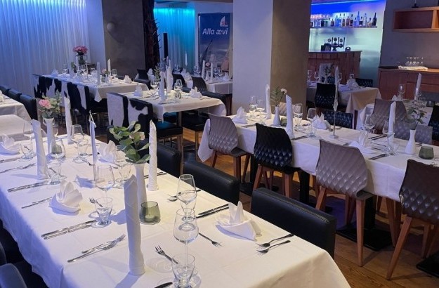 Venue setup at Isafold with long tables, gray and black chairs, white tablecloths, and glassware.