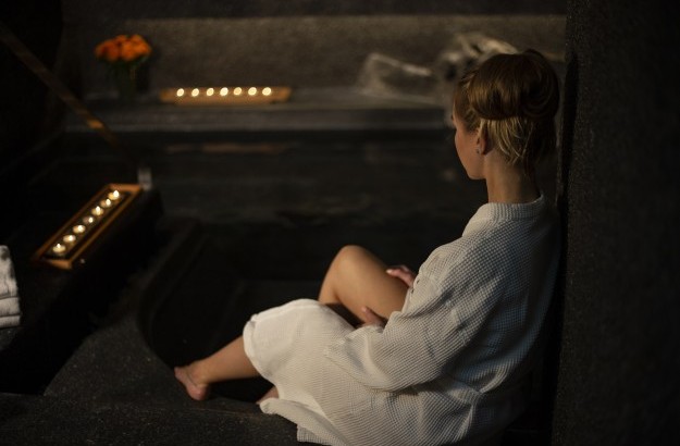 A young woman wearing a robe, sitting next to the hot tub at arnarhvoll spa. 