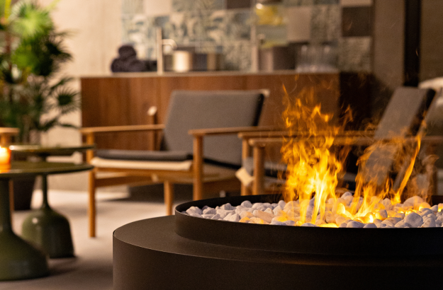 Fireplace with fire at the wellness are at Grandi spa. In the back are chairs, table and a candlelight.