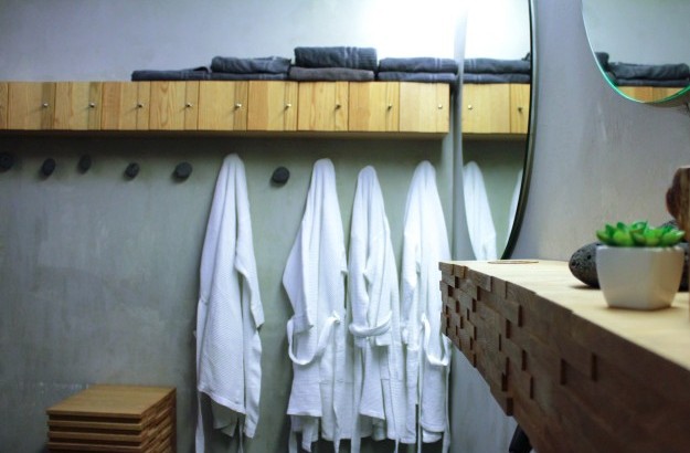 A few white bathrobes hanging up in a dressing room in isafold spa along with a few grey towels and mirrors hanging on the walls.