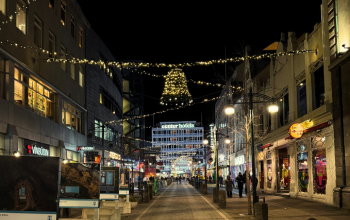 Göngugata í miðbæ Reykjavíkur að kvöldi, skreytt jólaljósum; í fjarska sést hús með “Center Hotels” skilti og fólk á gangi við verslanir.