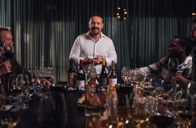 Wine tasting at Jorgensen Kitchen & Bar in Reykjavik with a sommelier dressed in white and guests sitting on each side of the table with bottles and glasses around.