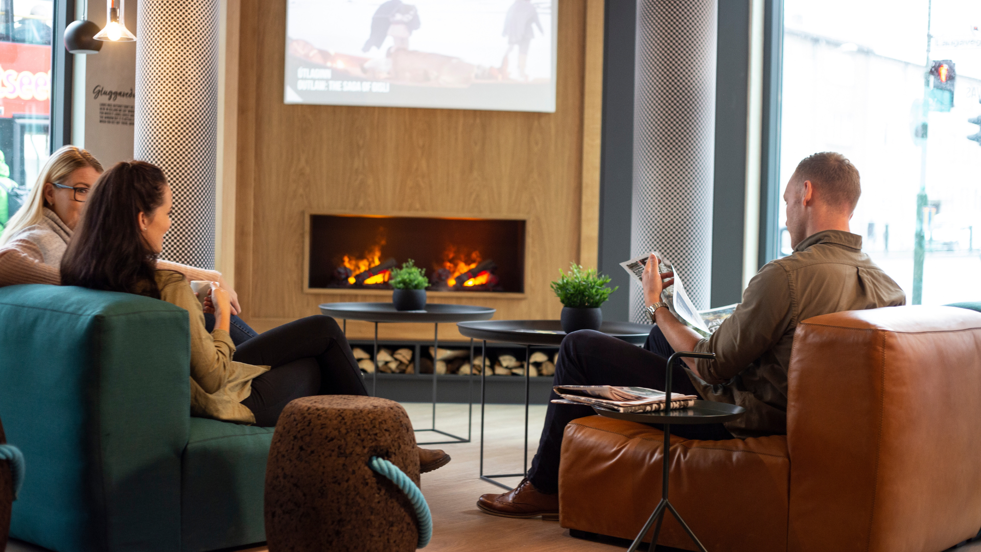 Three people sitting in the lounge of Center Hotels Laugavegur enjoying a cup of coffee and reading a newspaper.