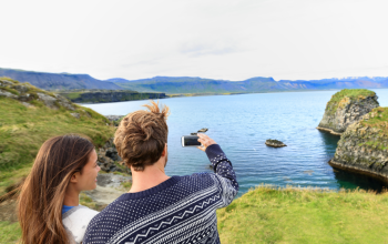 People standing in front of a mountain and lake view in Iceland, taking a picture with a camera dressed in Icelandic wool sweaters.