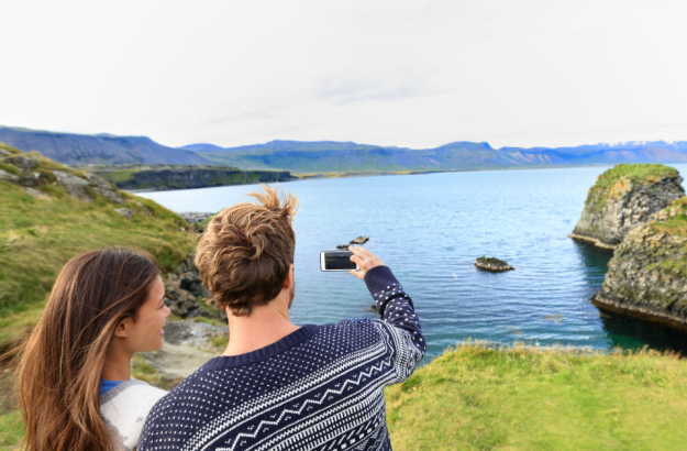 People standing in front of a mountain and lake view in Iceland, taking a picture with a camera dressed in Icelandic wool sweaters.