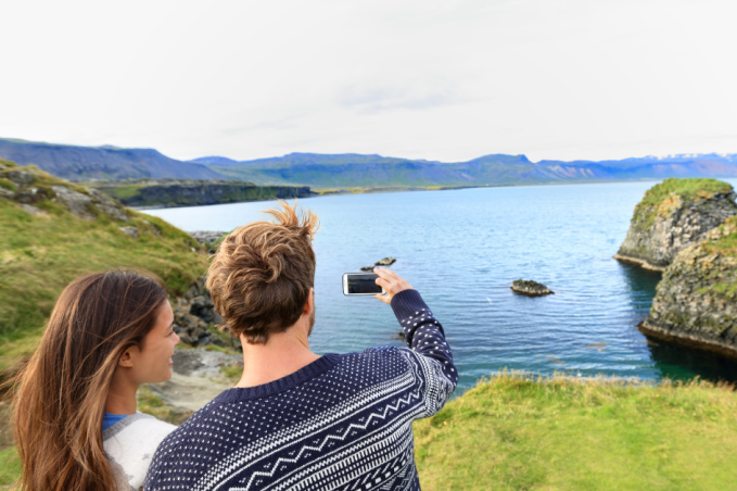 People standing in front of a mountain and lake view in Iceland, taking a picture with a camera dressed in Icelandic wool sweaters.