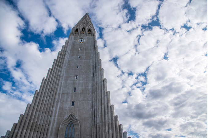 Hallgrimskirkja in the city center of Reykjavik seen from bottom up with blue sky and clouds visible.