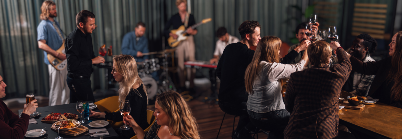 People enjoying food and drinks at Jörgensen kitchen and bar while a live band plays music in the background.