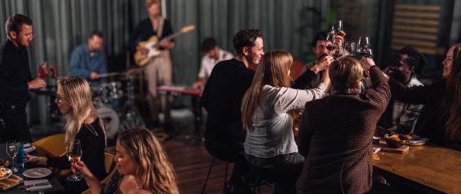 People enjoying food and drinks at Jörgensen kitchen and bar while a live band plays music in the background.